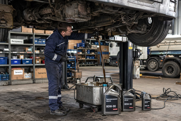 механик меняет трансмиссионное масло в грузовике в сервисе автопарка