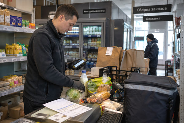 Сборщик продуктового онлайн-заказа сканирует товары в зоне dark store с холодильной секцией и пакетами для доставки