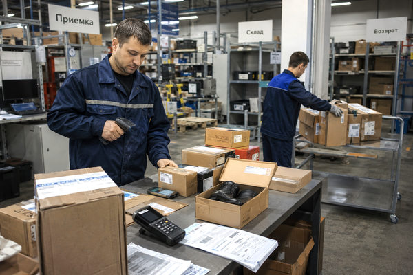 Сотрудники fulfillment-центра проверяют коробки с товарами для зарубежных онлайн-заказов в зоне приемки склада