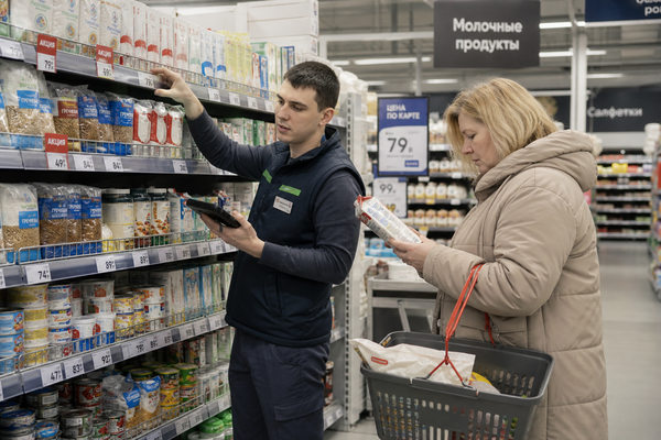 Сотрудник продуктового ритейла проверяет ценники на полке, покупатель сравнивает товары в супермаркете