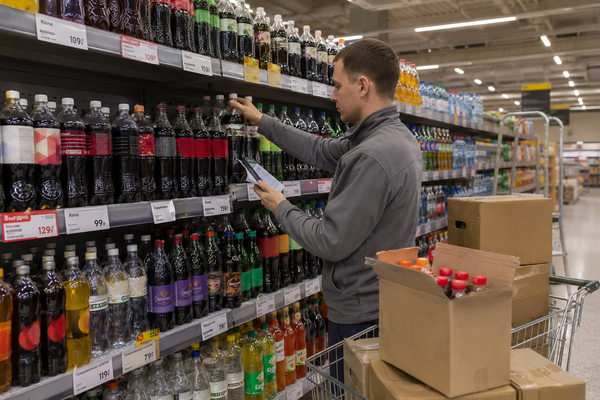 Сотрудник супермаркета проверяет выкладку колы и сладких газированных напитков на полке в российском ритейле