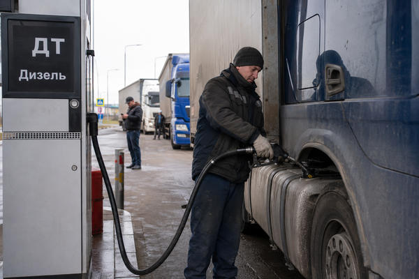 Водитель заправляет фуру дизелем на придорожной АЗС, где грузовики ждут очереди на дальний рейс