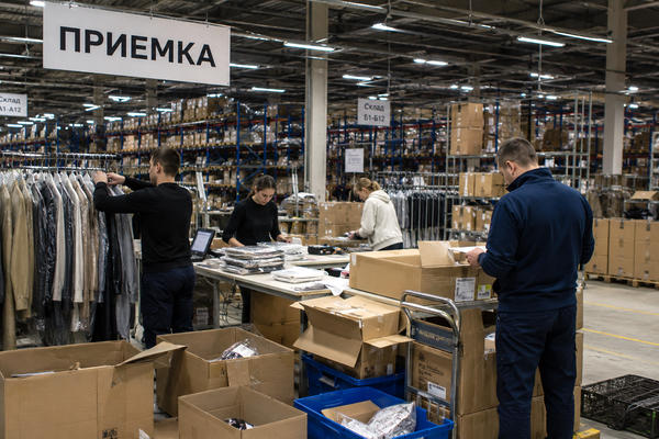 Сотрудники сортируют одежду в зоне приемки склада fashion-ритейлера на фоне коробок, рейлов и стеллажей