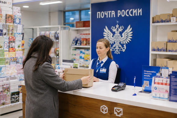 Сотрудница «Почты России» принимает посылку от представителя малой винодельни для отправки через онлайн-продажи
