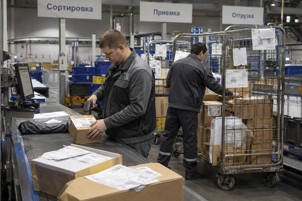 Сотрудник сортировочного центра сканирует посылку на линии обработки Почты России