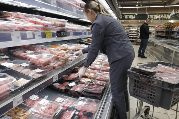 Сотрудник супермаркета выкладывает мясные полуфабрикаты и стейки в охлажденной витрине мясного отдела