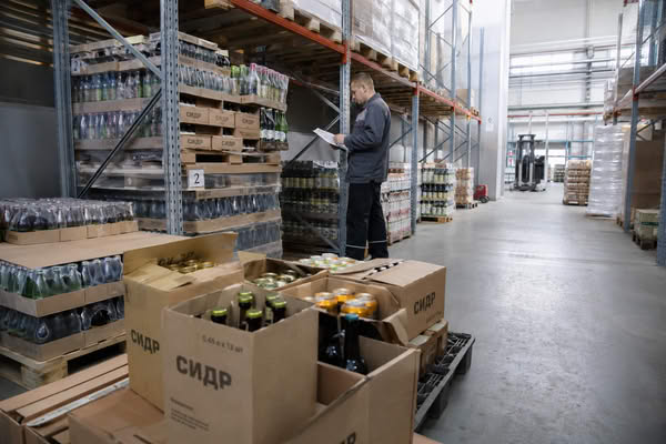 Склад готовой продукции с бутылками сидра и сотрудником предприятия, проверяющим ассортимент напитков