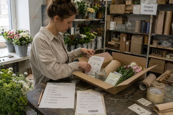 Сотрудница флористического магазина комплектует набор СТМ Flowwow с цветами, вазой и инструкцией по чек-листу