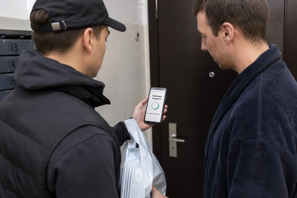 Курьер проверяет возраст получателя по смартфону перед передачей заказа на последней миле
