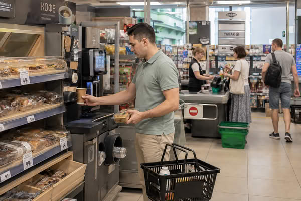 Покупатель берет кофе и выпечку у кофейной станции в продуктовом супермаркете