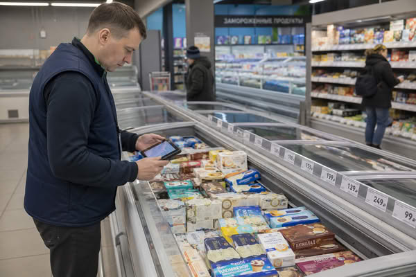 Сотрудник магазина проверяет ассортимент и цены на мороженое в морозильном ларе супермаркета