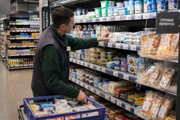 Сотрудник супермаркета выкладывает высокобелковые продукты на полку среди обычного молочного ассортимента