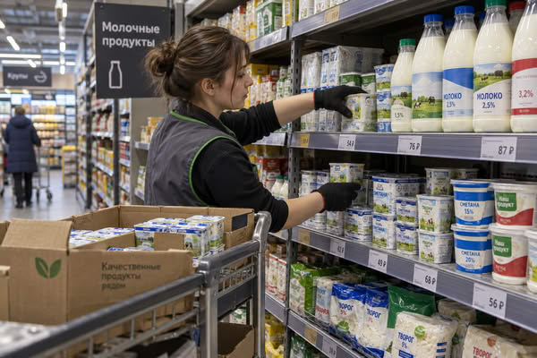 Сотрудница супермаркета выкладывает молочные продукты на полку в отделе FMCG