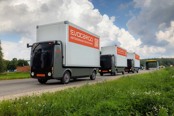 Колонна автономных робогрузовиков EvoCargo с надписью «автономная логистика» движется по загородной дороге в Подмосковье на фоне облачного неба и зелёного пейзажа