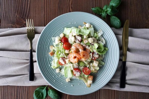 Салат Цезарь с креветками, томатами черри и хрустящими сухариками на сервированном столе; акцент на полезном белковом блюде и концепции здорового рациона.