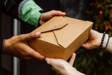 Курьер вручает клиенту заказ в крафтовой коробке — символ быстрой доставки и роста ожиданий покупателей