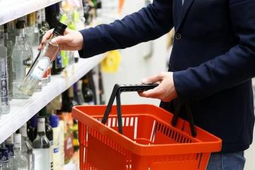 Покупатель выбирает бутылку водки в магазине с ограниченным ассортиментом алкогольной продукции