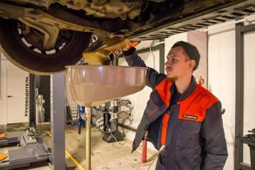 Механик заливает моторное масло в автомобиле на станции техобслуживания FIT SERVICE