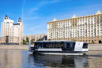 Современное речное электросудно движется по Москве-реке на фоне городских зданий, отражая развитие экологичного транспорта столицы